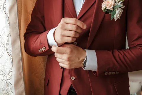 Un marié ajuste la manche de son costume bordeaux.