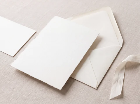 Illustration fictive : des cartes et enveloppes ivoire sur un tissu clair.