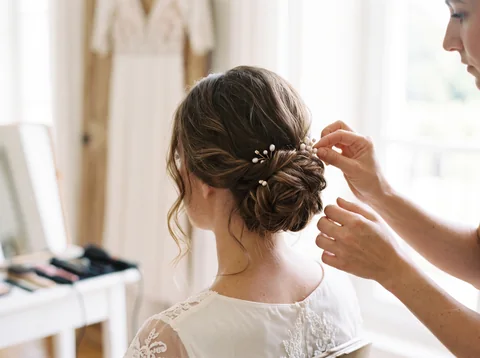 Illustration fictive : une coiffeuse ajuste le chignon bas d’une mariée.