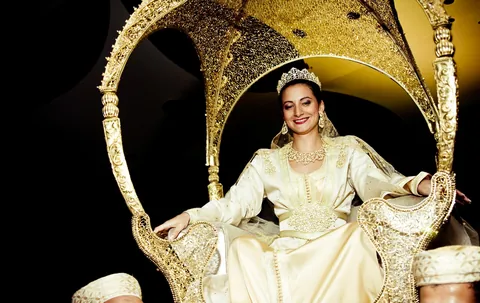 Mariée en tenue ivoire et dorée assise dans une amariya.